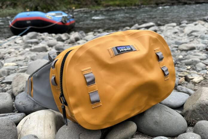 The Patagonia Guidewater waterproof hip pack sitting on rocks near the edge of a river with a raft in the background.