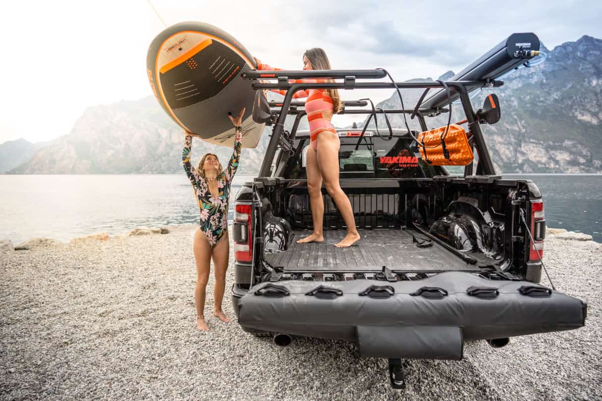 Two women unloading SUP from the top of a truck's crossbars.