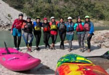 a group of woman kayakers pose for a group photo in their whitewater gear by a riverside in India