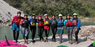 a group of woman kayakers pose for a group photo in their whitewater gear by a riverside in India