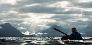 Oli Broadhead and his father cross open water in dappled light while kayaking the Inside Passage