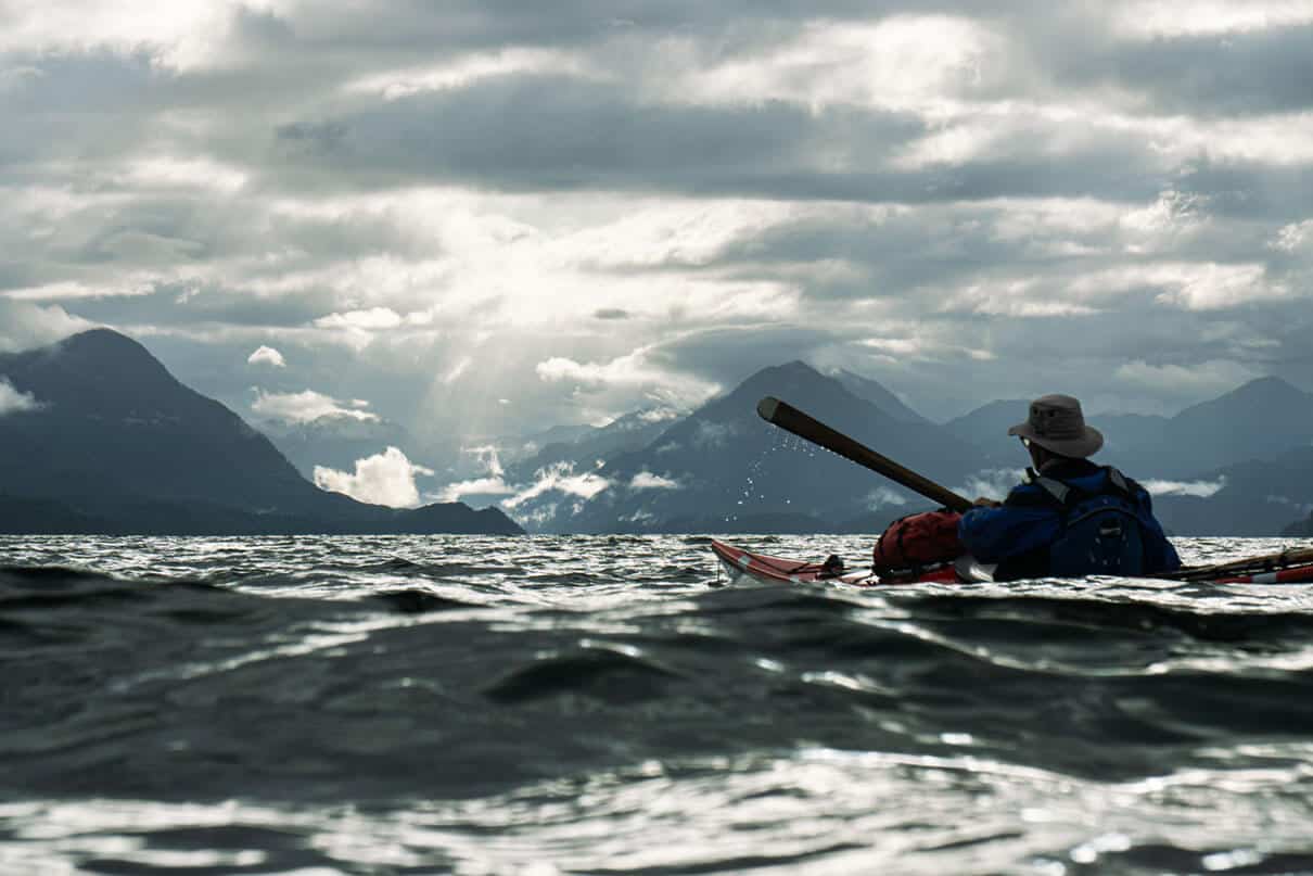 Oli Broadhead and his father cross open water in dappled light while kayaking the Inside Passage