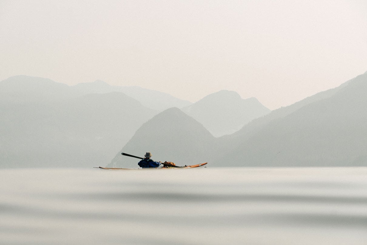 Kayaker paddles in front of wildfire haze over the mainland