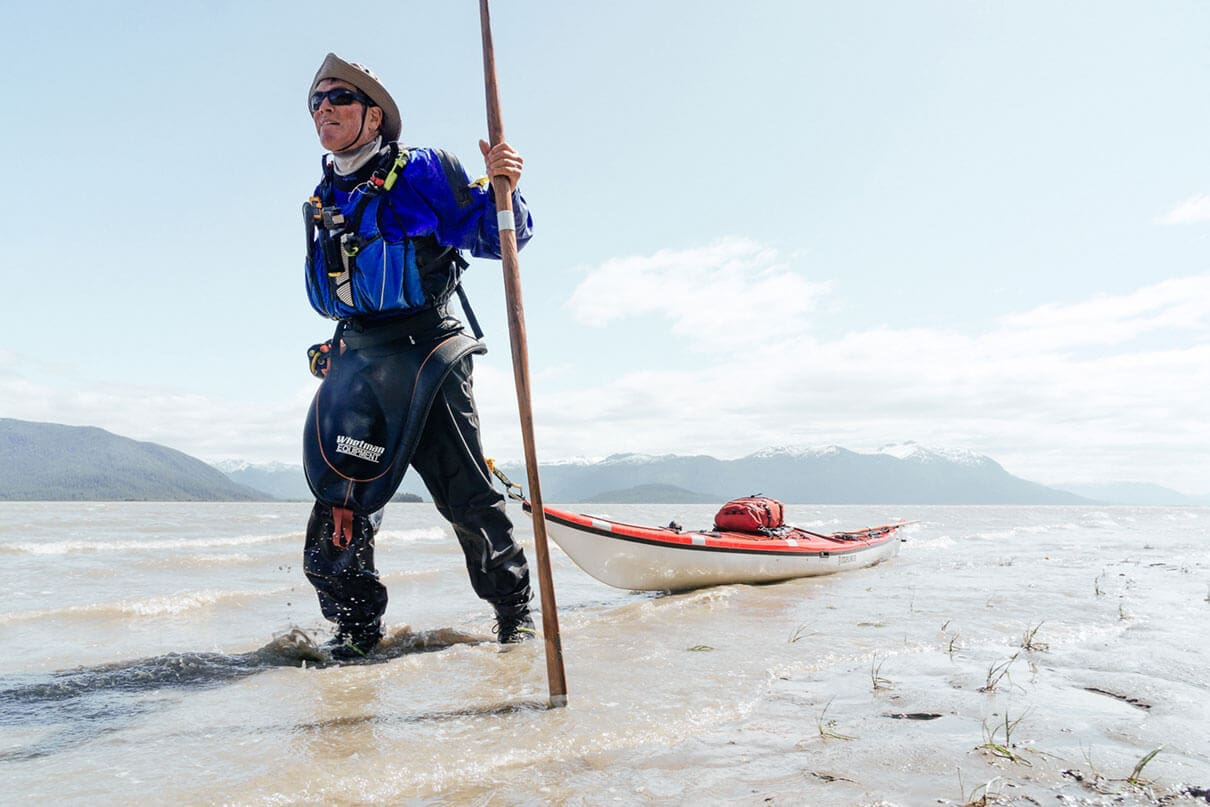 man in paddling gear pulls his sea kayak across tidal flats in the sun