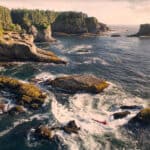 person paddles a kayak in cliffside surf on the Pacific Northwest coast
