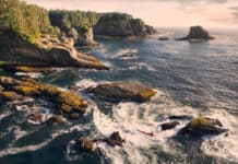 person paddles a kayak in cliffside surf on the Pacific Northwest coast