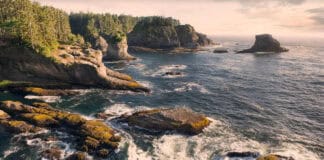 person paddles a kayak in cliffside surf on the Pacific Northwest coast