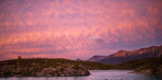 Two touring kayakers paddle in pink dawn or dusk light with mountains behind them
