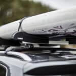 Best Paddleboard Car Racks For 2026 A paddleboard on top of a car's roof rack.