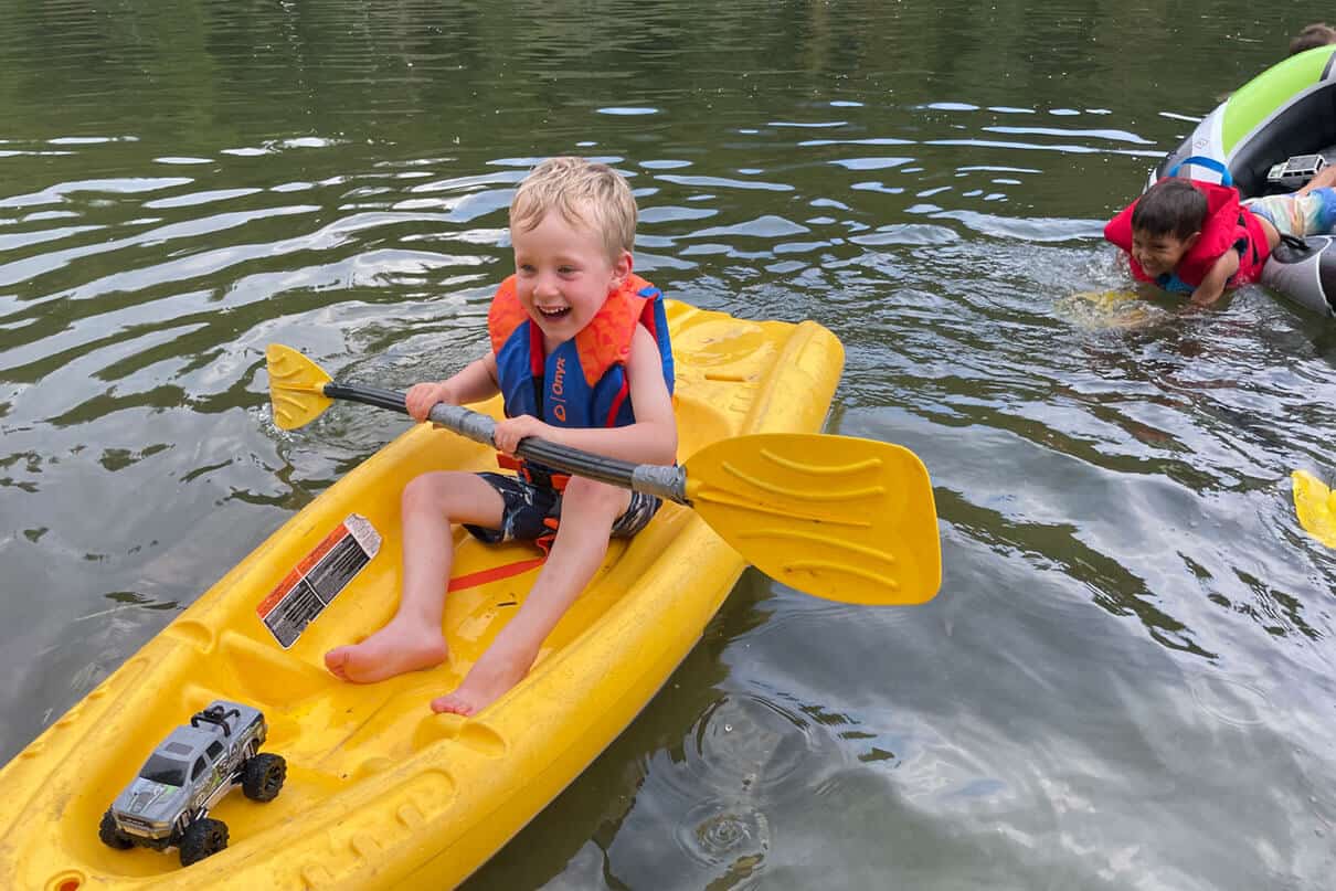 boy sits on a yellow child kayak while wearing an Onyx All Adventure life jacket