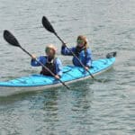 Best Tandem Kayaks For 2026 Two women paddling a tandem touring kayak.