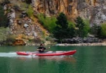Man paddles inflated kayak with V-hull across calm water.