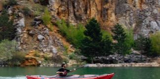Man paddles inflated kayak with V-hull across calm water.
