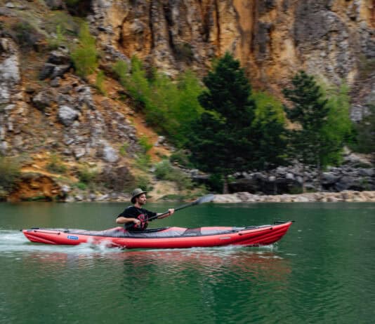 Man paddles inflated kayak with V-hull across calm water.