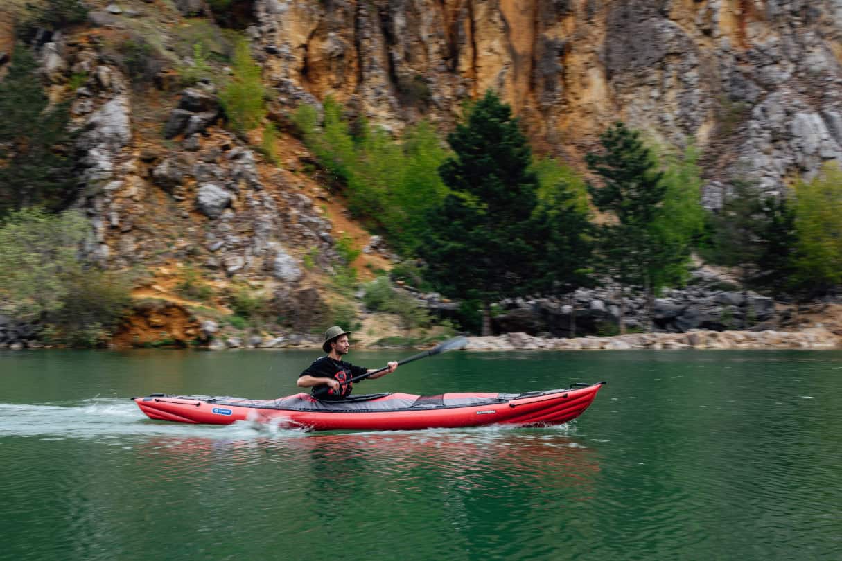 Man paddles inflated kayak with V-hull across calm water.