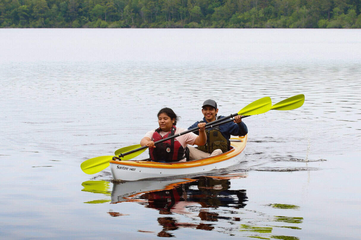 Two people paddling a tandem recreational kayak across a small lake.