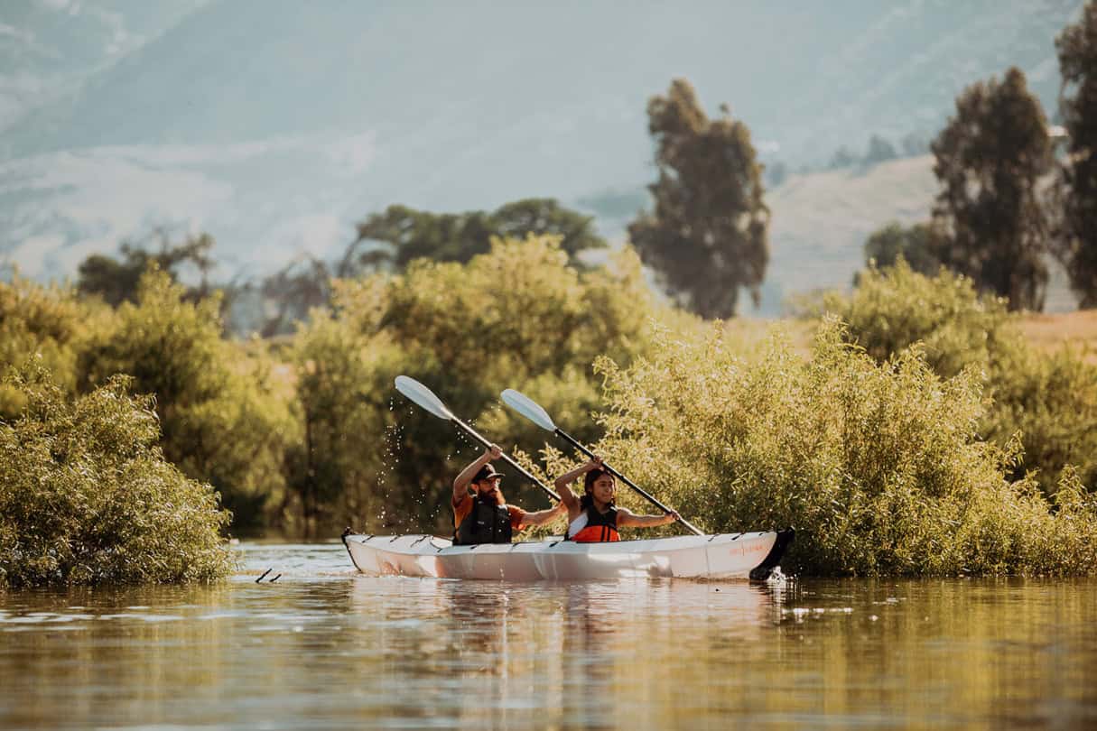 A pair in a two-person folding kayak on a stream.