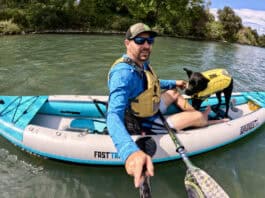 Man and dog in kayak on river.