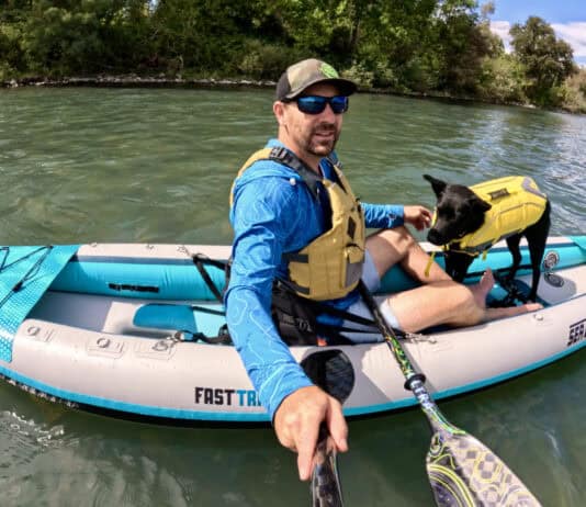 Man and dog in kayak on river.