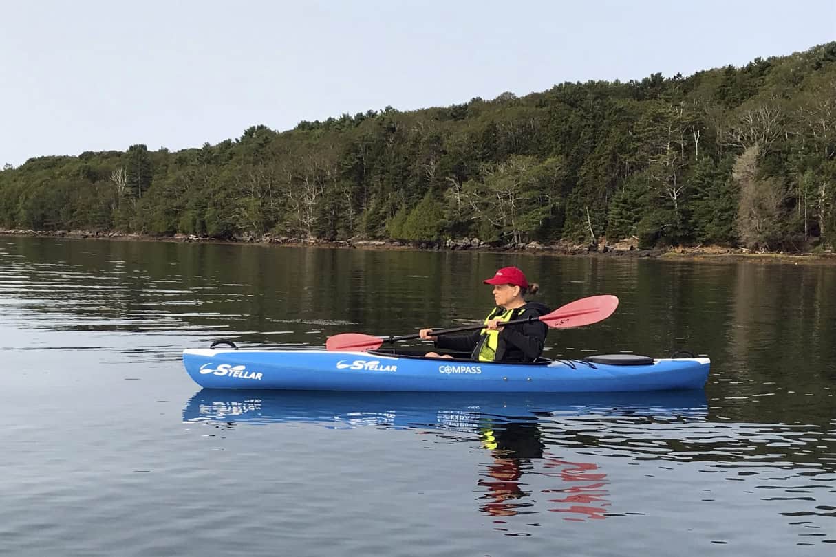 Woman paddling a blue recreational kayak on a lake.