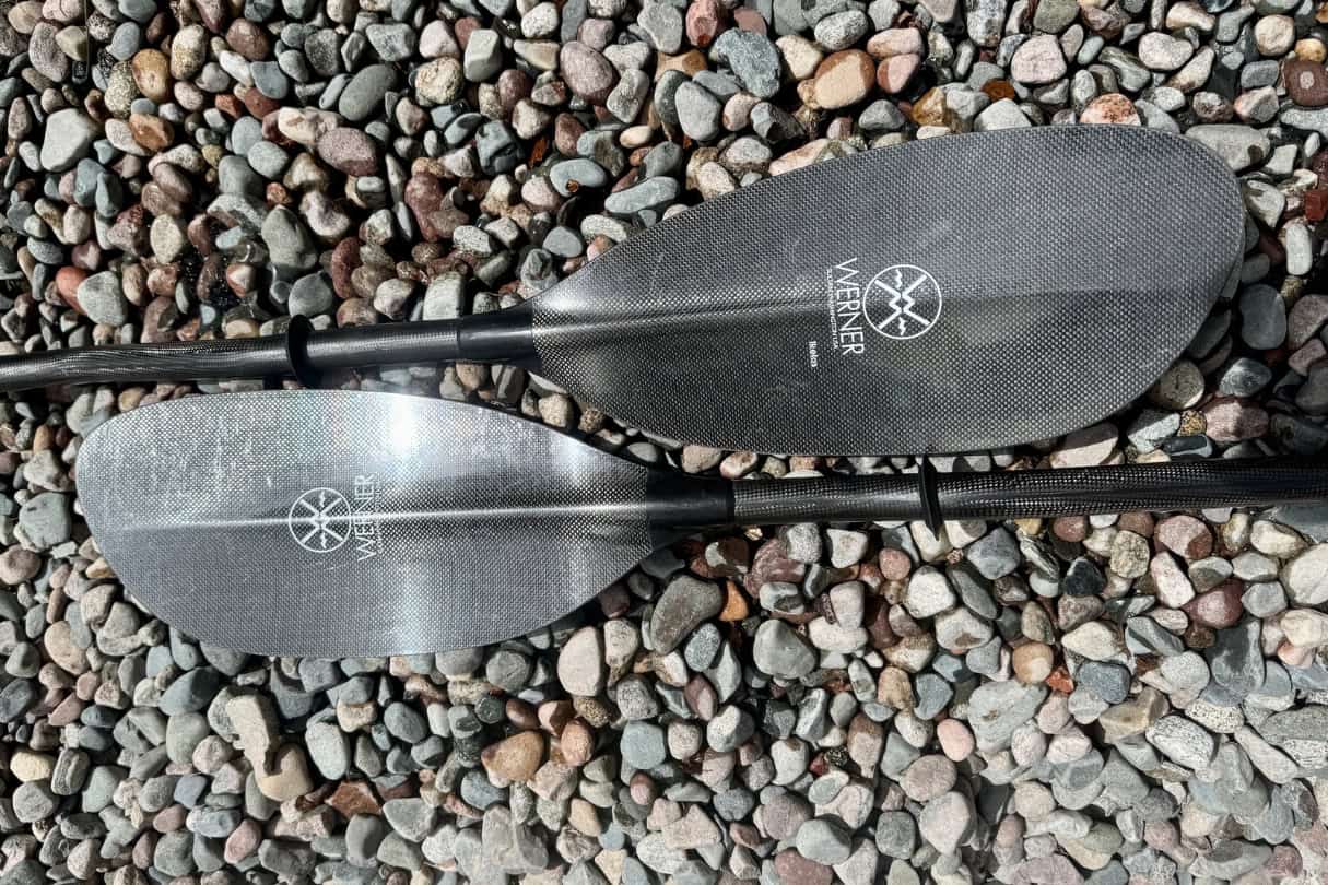 Two-piece carbon kayak paddle lying on rocks.