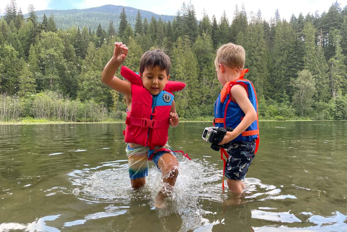 boy wears a Mustang Survival Lil Legends life jacket while playing with a friend in the river shallows