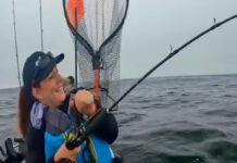 KC Kayak Fishing reels in a salmon in front of a humpback whale.