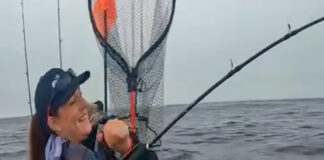 KC Kayak Fishing reels in a salmon in front of a humpback whale.