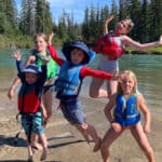 Best Child And Youth Life Jackets For 2026 a group of children and youth jump in the air beside a river while wearing a selection of life jackets