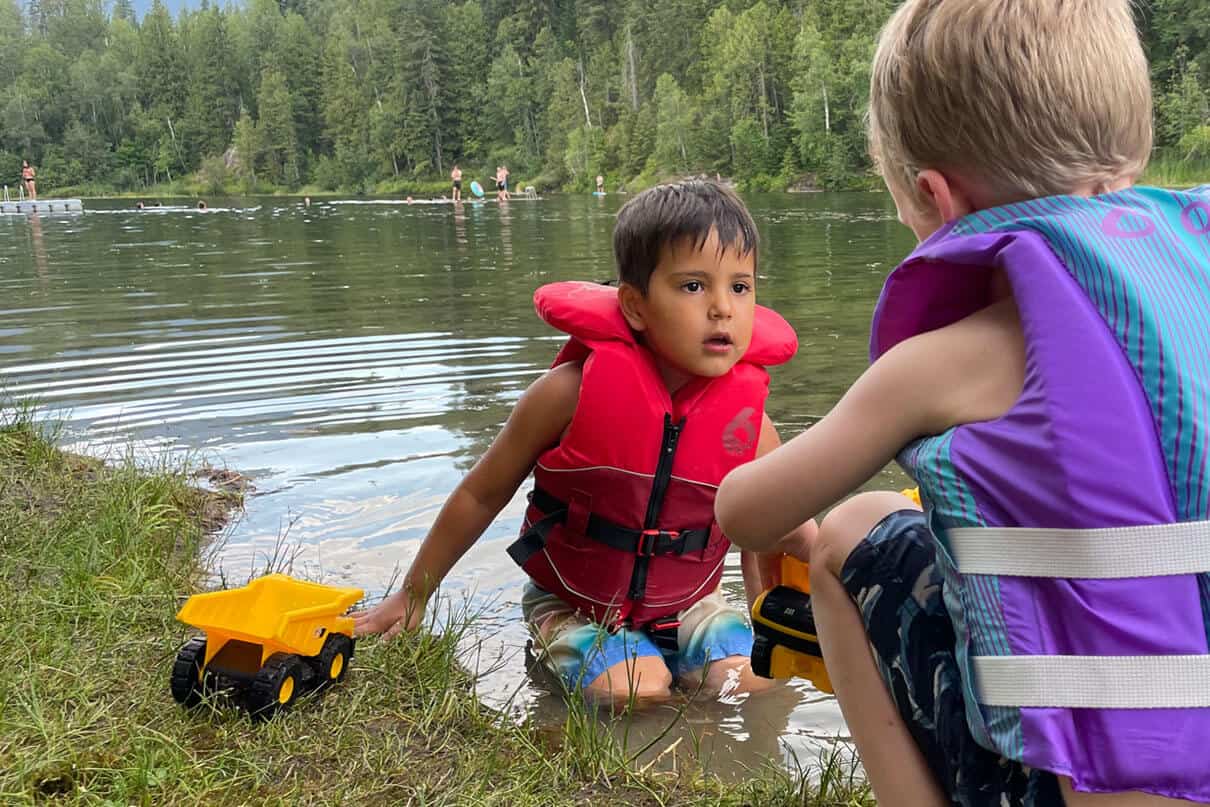 boy plays with toy truck and friend by the riverside while wearing a Level Six Stingray childrens life jacket