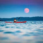 Former Adventure Kayak editor Virginia Marshall paddles her sea kayak in front of a harvest moon