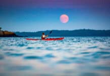 Former Adventure Kayak editor Virginia Marshall paddles her sea kayak in front of a harvest moon