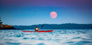 Former Adventure Kayak editor Virginia Marshall paddles her sea kayak in front of a harvest moon