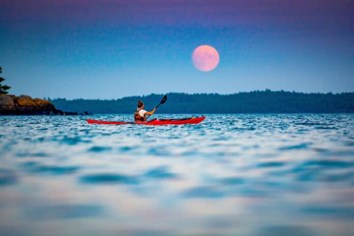Former Adventure Kayak editor Virginia Marshall paddles her sea kayak in front of a harvest moon
