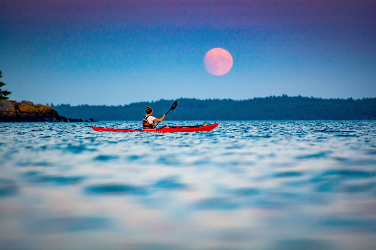Former Adventure Kayak editor Virginia Marshall paddles her sea kayak in front of a harvest moon