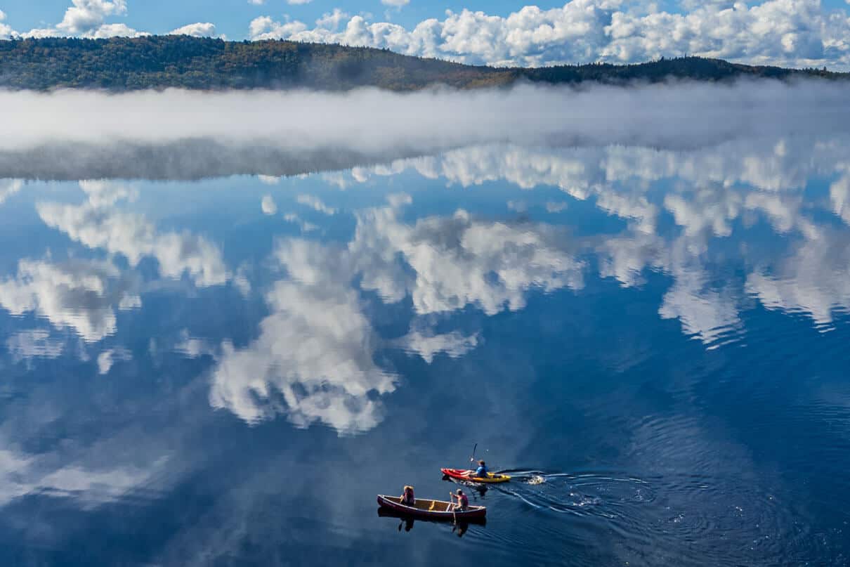 bird's eye view of a canoe and kayak paddling across still water with mountains and clouds reflected