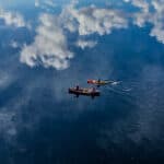 bird's eye view of a canoe and kayak paddling across still water with mountains and clouds reflected