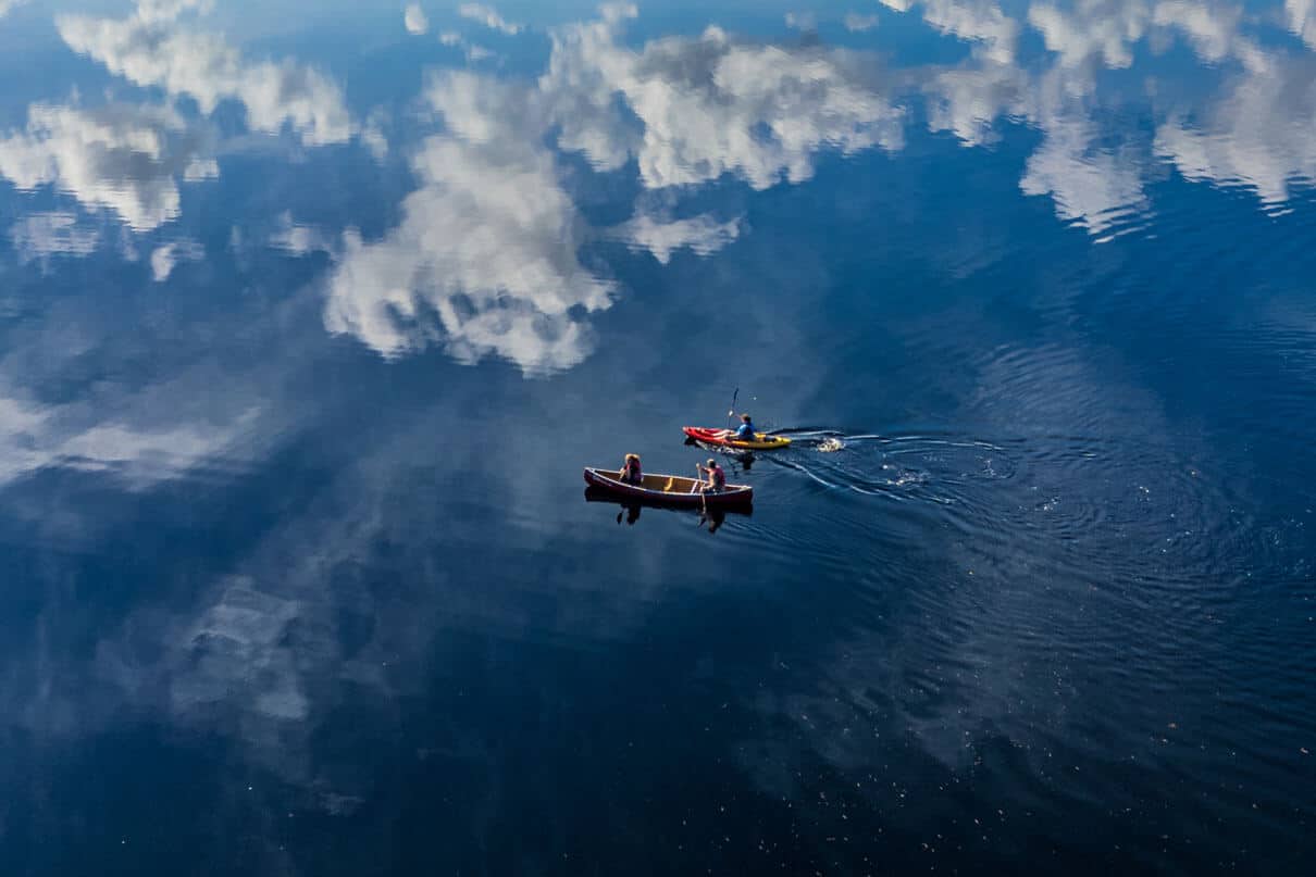 bird's eye view of a canoe and kayak paddling across still water with mountains and clouds reflected
