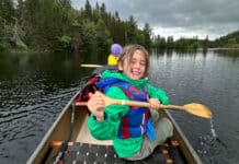 First Canoe Camping Owen Morris poses with paddle while canoeing under cloudy skies on his first canoe camping trip