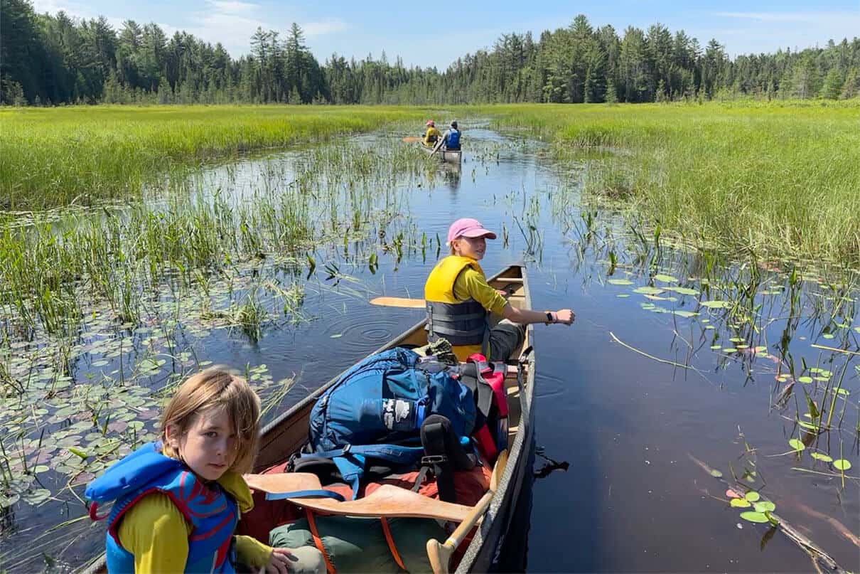Owen Morris and his family paddle two canoes through a small, grassy body of water