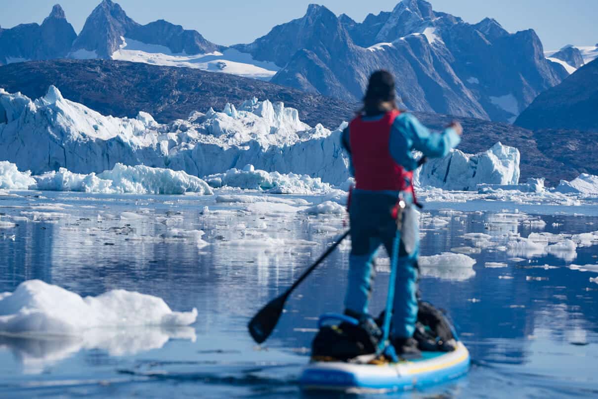 paddleboarder pilots his board across the fjord with ice all around