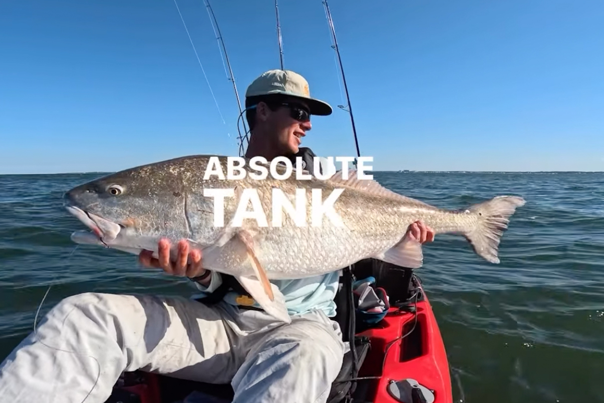 Image of Ethan Sommer holding a massive redfish in a fishing kayak