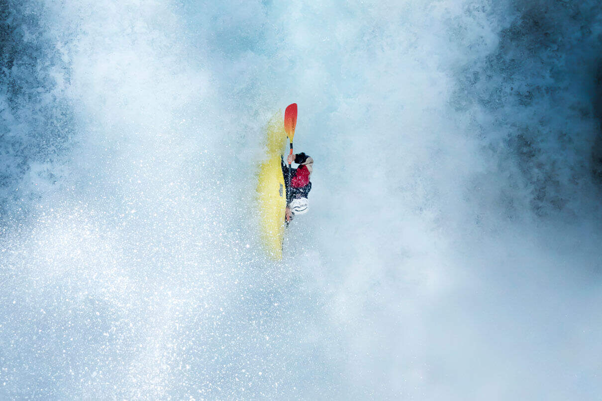 whitewater kayaker moves straight down in the midst of waterfall spray