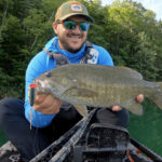 Best Smallmouth Bass Lures For 2026 Man holding smallmouth bass hooked with a large fishing lure.