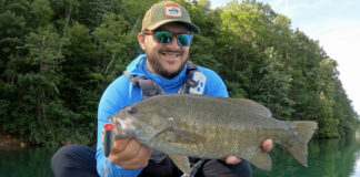 Best Smallmouth Bass Lures For 2026 Man holding smallmouth bass hooked with a large fishing lure.