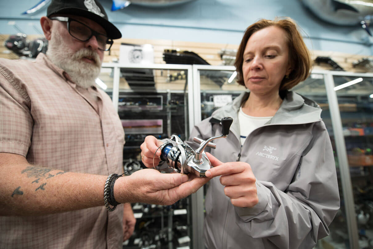 a tackle shop manager shows off a Shimano real to a prospective customer