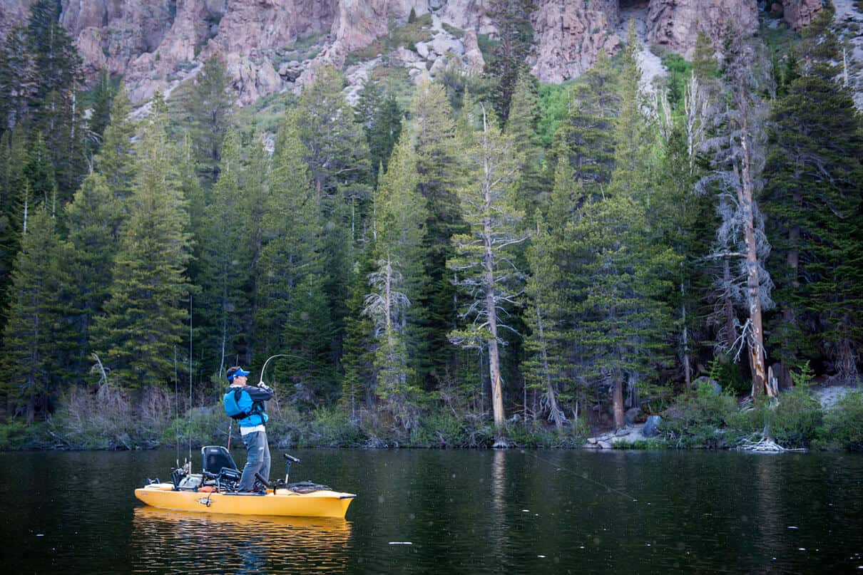 man stands and casts from a Hobie fishing kayak on a forested lake