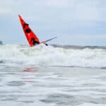 Deb Volturno On The Future of Sea Kayaking The bow of Deb Volturno's red kayak rising over the surf