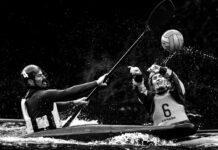 black and white photo of two kayakers in the water swinging paddles at a ball while they play kayak polo