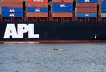 How The Sweeping Trade War Is Hitting Paddlesports From All Sides kayaker paddles in front of a cargo ship loaded with shipping containers
